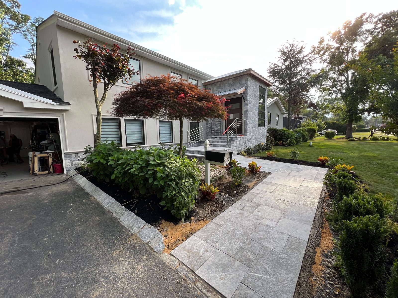 Completed modern home entrance by Sioux Masonry & Pavers — stone-veneered façade, travertine paver walkway with granite curbing, and fresh landscape borders in Central New Jersey
